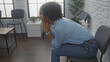 © Krakenimages.com - A beautiful young african american woman with curly hair sits thoughtfully in a modern waiting room with a minimalist interior design.