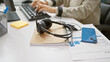 © Krakenimages.com - Focused, mature woman typing on a computer in a modern office with headphones and a smartphone on her desk.