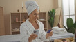 © Krakenimages.com - Woman enjoying wellness spa indoors while using phone and credit card in a serene beauty center room with a towel on her head and wearing a bathrobe.