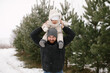 © VikaNorm - A small child in a white jumpsuit sits with his father on a post in the winter, near a pine forest.