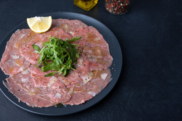 Marbled beef carpaccio with arugula, parmesan cheese, olive oil and lemon. A traditional classic appetizer made from thinly sliced raw meat. Close-up, selective focus, black background.