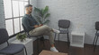 © Krakenimages.com - Hispanic man waiting in an indoor lobby with a beard and casual attire, sitting comfortably and using his phone, surrounded by modern decor and empty chairs.
