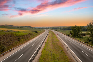 Deserted highway at sunset with vibrant skies and lush green landscapes on either side.