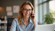 © PREM - Smiling mature middle aged professional business woman manager talking on the cell phone in office using laptop computer