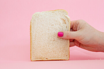 freckled hand with pink painted nail hold a slice of white bread against a pink background