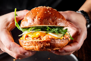 A close-up of a hand holding a gourmet burger with fresh greens, melted cheese, and a juicy patty on a sesame bun. Perfect for food blogs, restaurant menus, or culinary magazines.