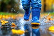 © Lux Images - Child in Blue Rain Boots Splashing Through Puddle with Autumn Leaves