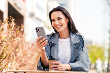 Wall Mural - Photo of charming positive woman wear grey trench chatting instagram twitter telegram facebook sitting cafeteria outdoors urban city street