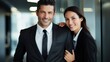 © Iona - A professional-looking man and woman in business attire stand side by side, smiling confidently in a modern office environment.