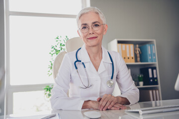 Poster - Photo of beautiful professional senior doc lady friendly smiling sit table patient consultation wear white lab coat office clinic indoors