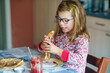 © Irina Schmidt - Cute little girl having crepes for breakfast at sunny kitchen. Happy child eating healthy pancakes with strawberry jam