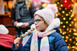 © Irina Schmidt - Little cute girl eating white chocolate covered strawberries on skewer on traditional German Christmas market. Happy child on traditional family market in Germany during snowy day