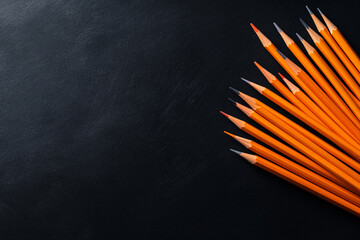 A black background with a row of pencils on it. The pencils are all orange and are lined up