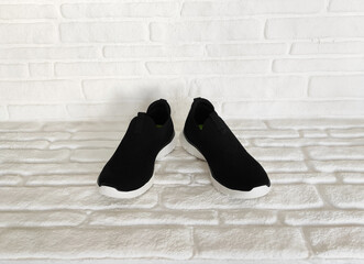 Black sports sneakers with laces on a white brick background