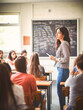 © Aqsapics - a school classroom facing the whiteboard. Female teacher with black hair writing on the whiteboard with a whiteboard marker. Students facing the front of the classroom.