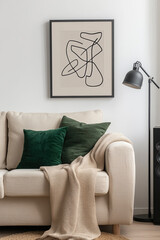 Sticker - A minimalist, black frame with an abstract line drawing of interconnected shapes hangs on the wall above a beige sofa adorned with emerald green pillows and a blanket.