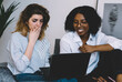 © BullRun - Smiling african american young woman and caucasian hipster girl shocked with last fashion news on website, millennial diverse friends watching video on laptop computer using high home internet