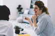 © BullRun - Happy smiling hipster girl laughing during coffee time with hosting friend while sitting at table in comfortable stylish apartment, carefree female talking with woman during leisure indoors