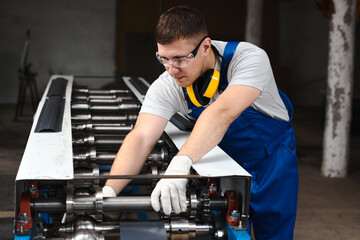 Professional engineer man in blue uniform works in factory. Rolled metal, metal processing and manufacturing of metal fence