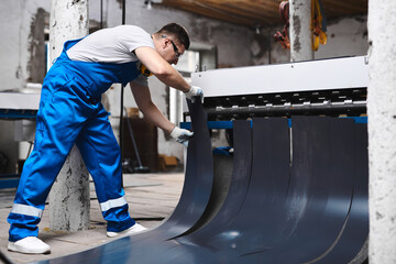 Professional engineer man in blue uniform works in factory. Rolled metal, metal processing and manufacturing of metal fence