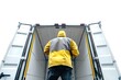 © Alena - A person in a yellow jacket standing near the back of a vehicle, suitable for use in images related to work, transportation, or outdoor activities