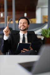 Sticker - A man in a suit is sitting at a desk with a notebook and a pencil. He is smiling and holding the pencil up in the air. The scene suggests that he is in a creative or problem-solving mindset