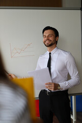 Wall Mural - A man in a white shirt and black pants is standing in front of a white board with a graph on it. He is smiling and holding a piece of paper. Concept of professionalism and confidence