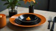 © Kasper - Sleek dining arrangement with an orange plate, black utensils, and a fresh orange.