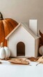 © lililia - A charming white wooden house model is beautifully displayed alongside vibrant autumn leaves and decorative pumpkins, creating an inviting seasonal decor arrangement