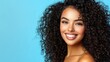 © яна винникова - Joyful young woman with curly hair smiling brightly against a vibrant blue background in a studio setting