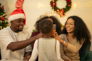 A lively Christmas celebration with three african friends enjoying drinks and holiday cheer on a sofa. The festive atmosphere includes Christmas trees, wreaths, lights, and decorations.