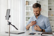 © Anastasiya - A man is focused on adjusting a microphone attached to his shirt in a well-lit office. He seems prepared for an online presentation, showcasing a professional environment.