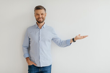 A man stands confidently with one hand extended, smiling warmly. He wears a light blue shirt and jeans, exuding positivity in a contemporary indoor environment.