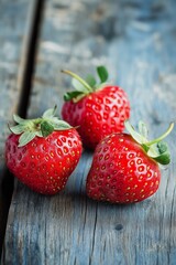 Wall Mural - Three vibrant red strawberries are placed on a weathered blue wooden surface, contrasting beautifully in this close-up shot.