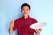 © Muhamad  - Young Asian man give thumb up and showing happy expression while holding empty dinner plate