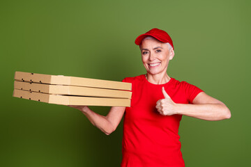 Poster - Photo of pretty senior female professional delivery employee pizza thumb up wear red uniform workwear isolated on khaki color background