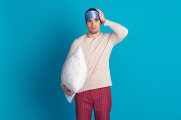 Wall Mural - Portrait of nice young man hold pillow wear pajama isolated on blue color background