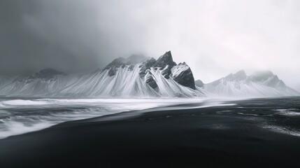 Dramatic black sand beach with shrouded mountains and waves crashing in a moody, monochromatic landscape.