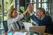 © KirKam - Professional Caucasian man and woman celebrating success with a high-five in a modern office setting, expressing teamwork and achievement.