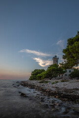 Wall Mural - Beautiful sunset in a landscape on a rocky coast with a striking lighthouse and pine forest. View over the coast to the building, on the Mediterranean, Vir, Dalmazien, Croatia, Adriatic