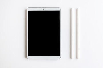 A white tablet with a blank black screen is placed on a white surface next to two white styluses, creating a minimalist and modern composition