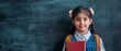 © Evgeniya - A little cute smiling Indian schoolgirl girl with a backpack and a book in her hand. Studio photo on the background of a dark blackboard with a place for text. Elementary school, back to school.