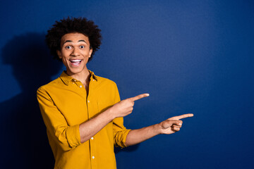 Wall Mural - Portrait of nice young man point fingers empty space wear yellow shirt isolated on dark blue color background