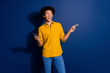 Canvas Print - Portrait of nice young man smart phone indicate finger empty space wear yellow shirt isolated on dark blue color background