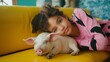 © Zography - Little girl in pink pajamas with black patterns lies next to a cute sleeping pig on a yellow couch.