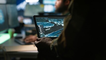 Army telecommunication systems operator using satellite software on tablet, providing combat support. Military dispatcher managing communications networks, with portable device, camera A