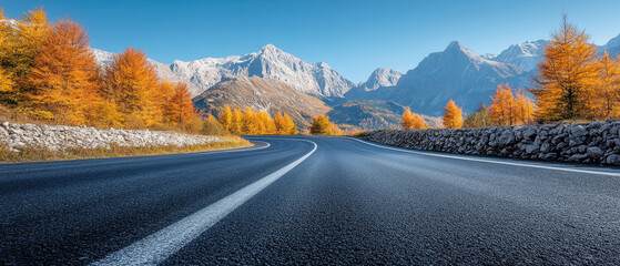 A road with a mountain in the background. The road is empty and the sky is clear. The road is lined with trees and the leaves are changing colors