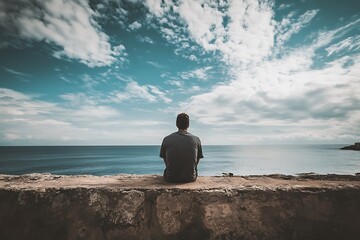 Silhouette of man sitting on a wall overlooking the ocean, cloudy sky, and blue sky