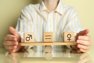 Wall Mural - Gender equality concept. Woman with wooden cubes of male and female symbols on scales at table, closeup