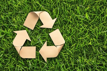 Cut-out of recycling symbol made from kraft paper on green grass. Eco-friendly design concept promoting conservation and reduction of waste. Biodegradable paper shape on natural lawn.